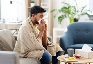 Man on sofa blowing nose with tissue. sicknote.com. He appears unwell